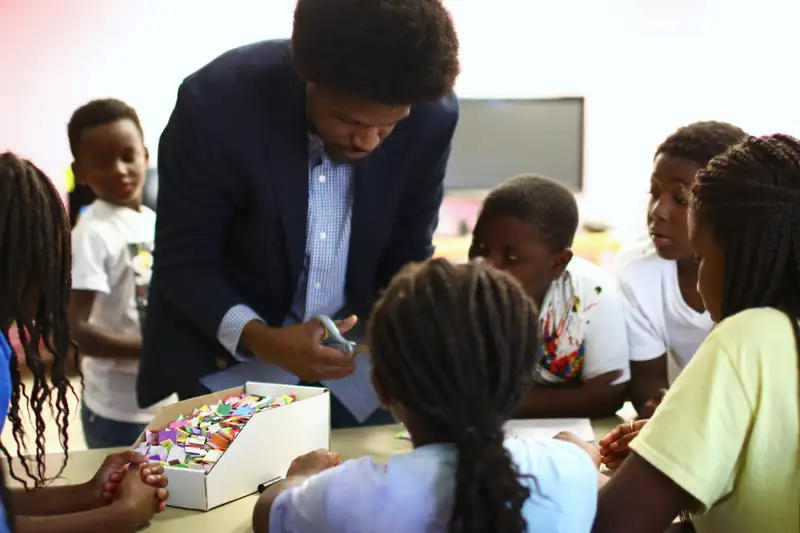 A mentor shows a table of children how to build with foam shapes