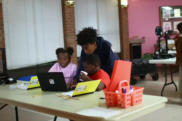 Children program at a laptop as a mentor leans in