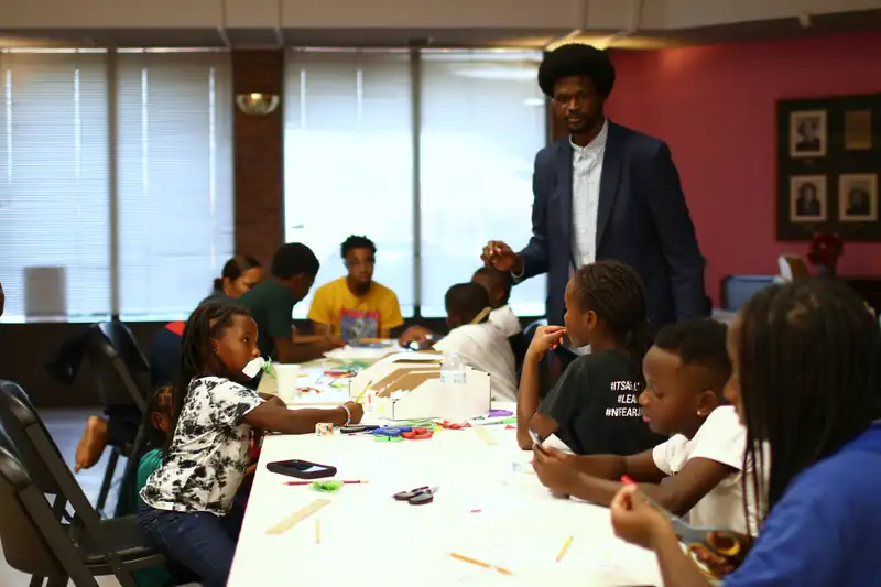 A full table of children builds while a mentor helps