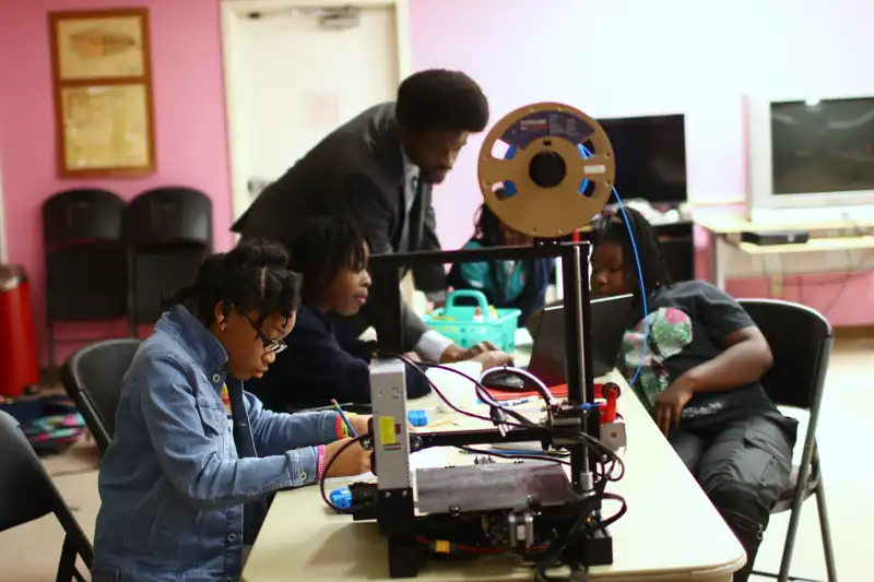 Students gather round a 3D printer with a mentor