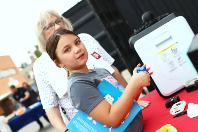 A girl smiles beside a 3D printer at the table