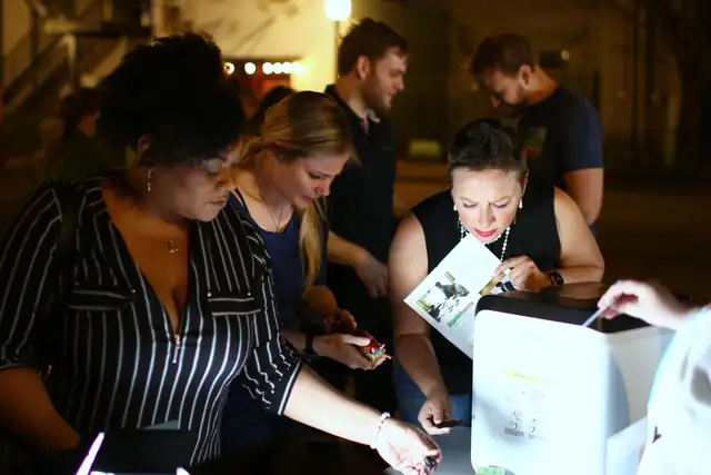 Grown-ups lean in over a lit bookmark circuit after dark