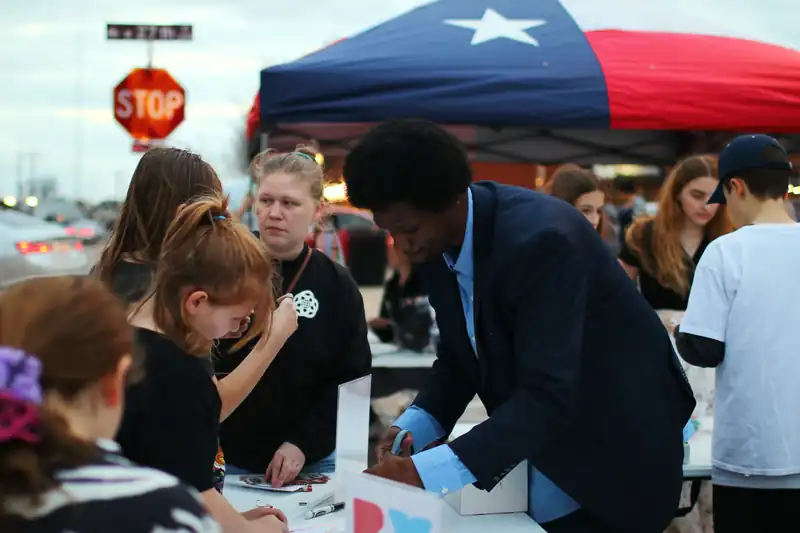 A mentor helps children under a festival tent at dusk