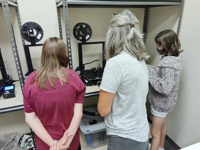 Students watch a 3D printer build their part