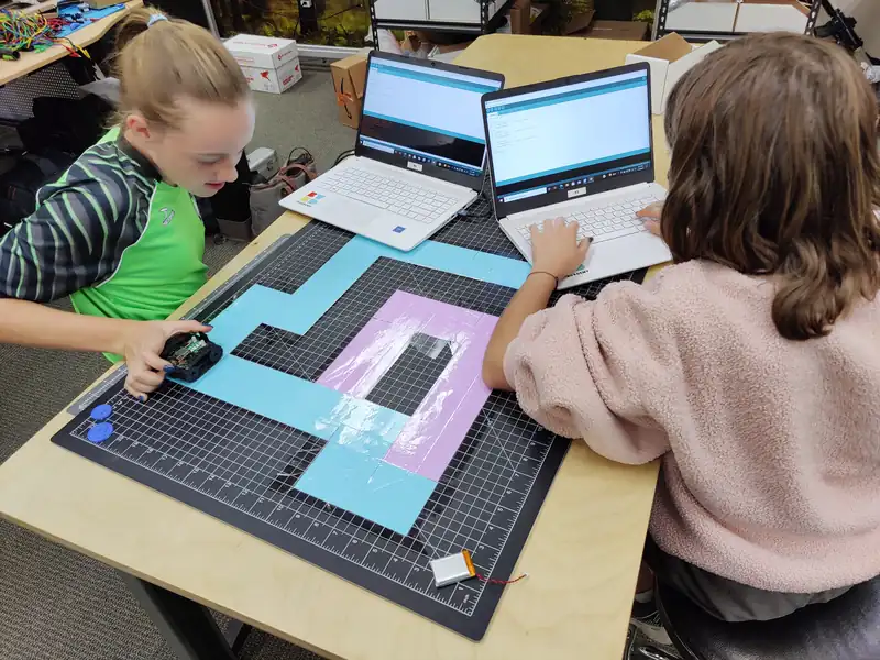 Two students program a robot to drive a taped maze