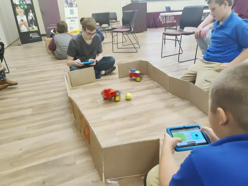 Students drive robots with tablets inside a cardboard arena