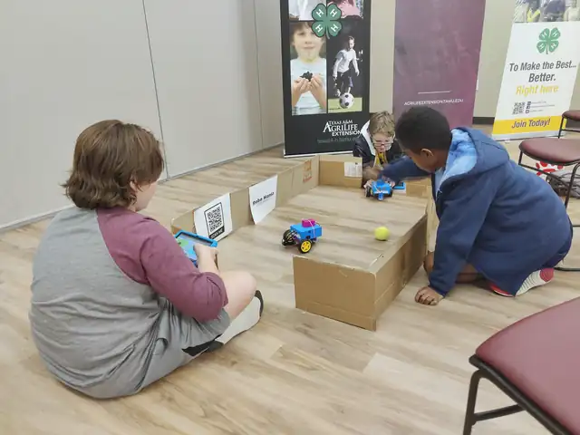 Two students steer robots across the floor