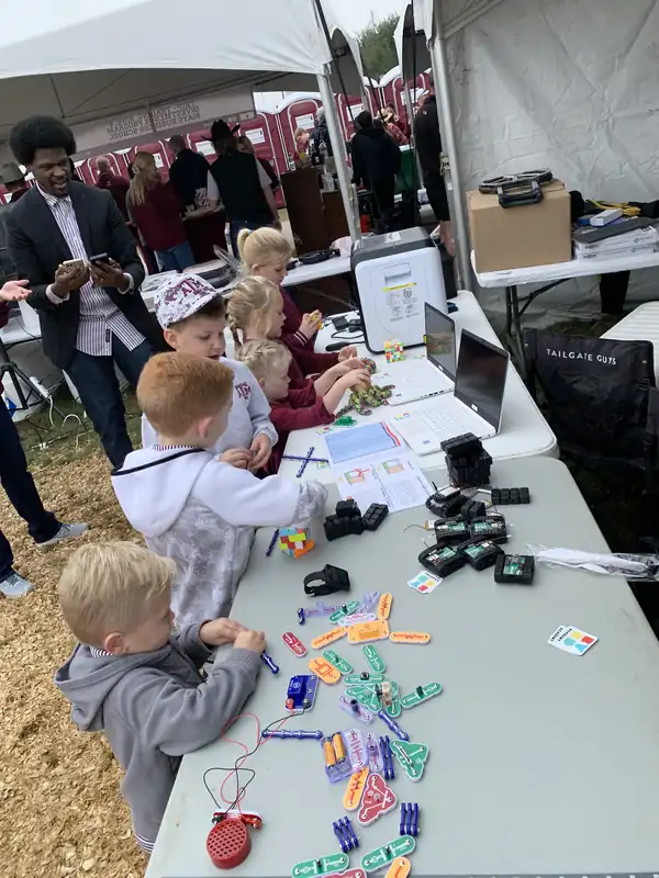 Children gather at a table of circuit parts before kickoff